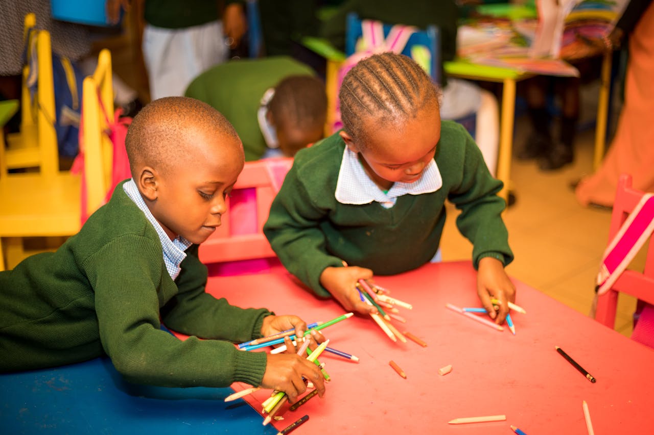 Two children at a table in a classroom, engaged in creative activities with colored pencils.