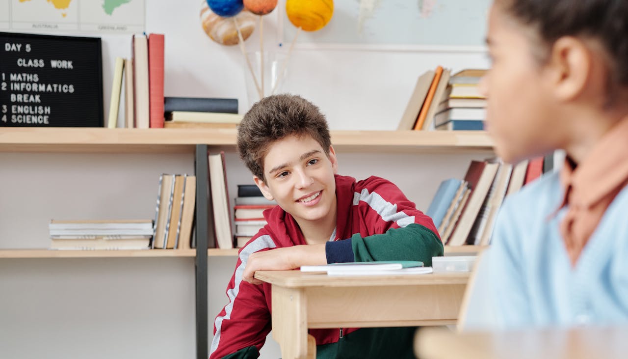 Teenagers smiling and interacting in a school classroom setting with books and educational materials.